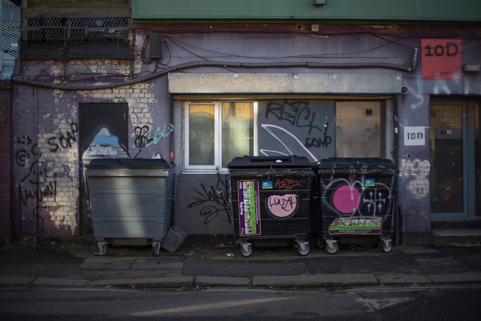 The image depicts a section of an urban building facade with a weathered brick wall partially painted in purple, featuring visible graffiti tags and markings in various colors including black, white, 
